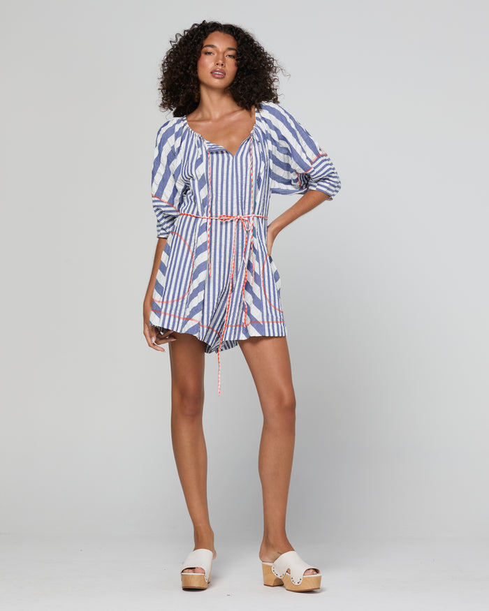 A woman modeling a blue, white, and red striped romper with puff sleeves and a tie waist