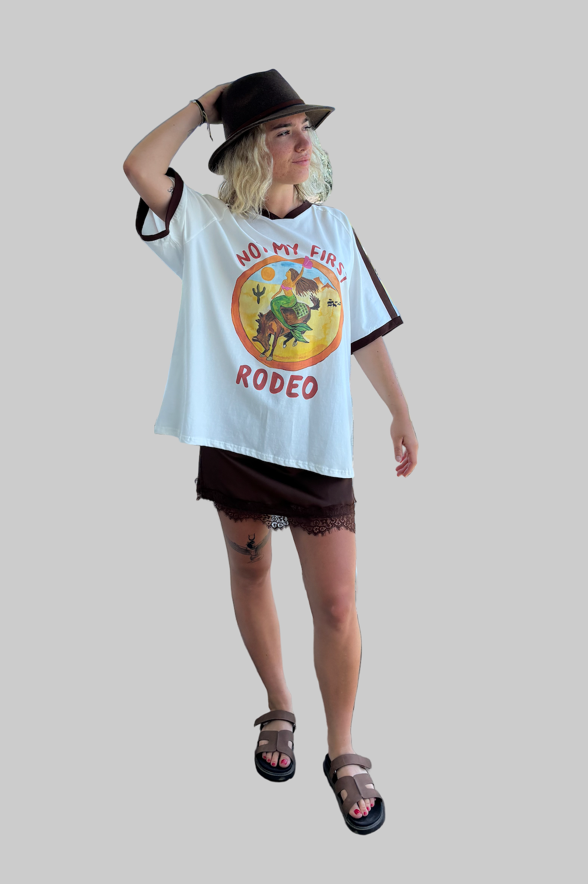 not my first rodeo tee by frankie is a white cotton tee with a mermaid riding a horse in a desert sccene with contrast sleeve stripes
