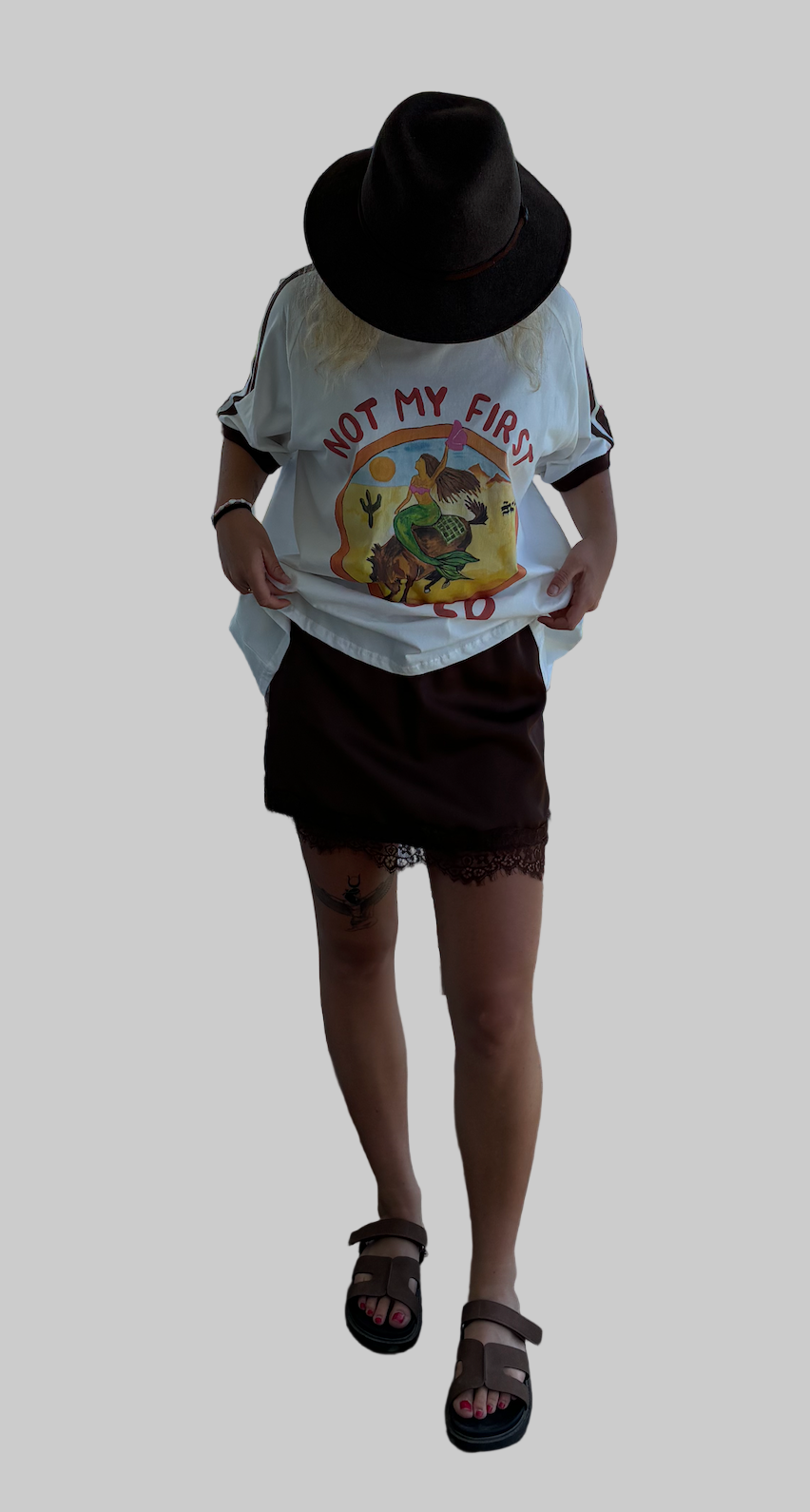 not my first rodeo tee by frankie is a white cotton tee with a mermaid riding a horse in a desert sccene with contrast sleeve stripes