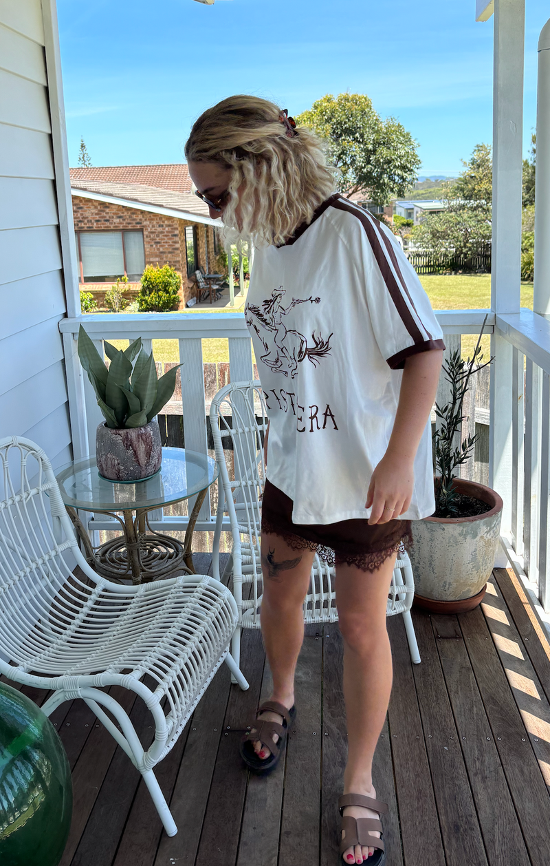 pistolera tee in white by frankie is a cotton t-shirt with a image of someone shooting while riding a horse